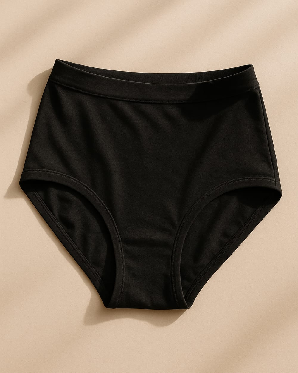 Black organic cotton high-rise brief on a warm neutral background showing soft jersey knit fabric